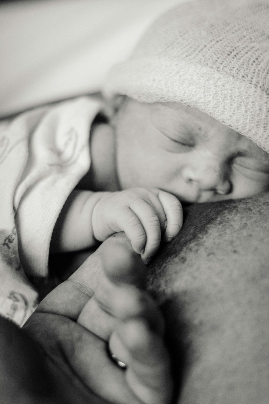 Black-and-white close photograph of a newborn holding an adult finger