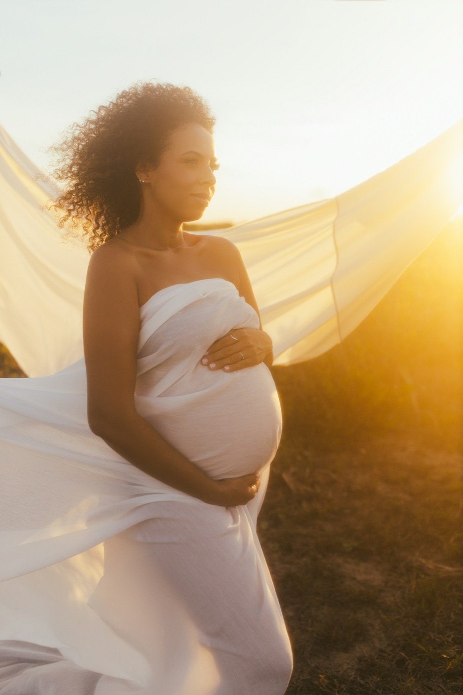 Expectant mother in flowing white fabric at golden hour