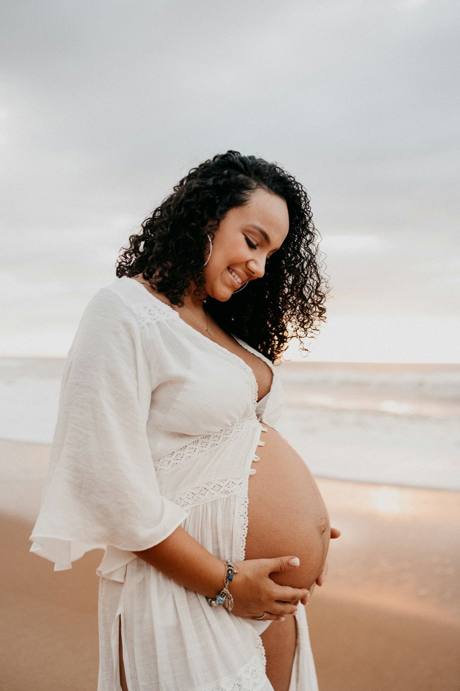 Expectant mother in white by the sea beneath an open sky