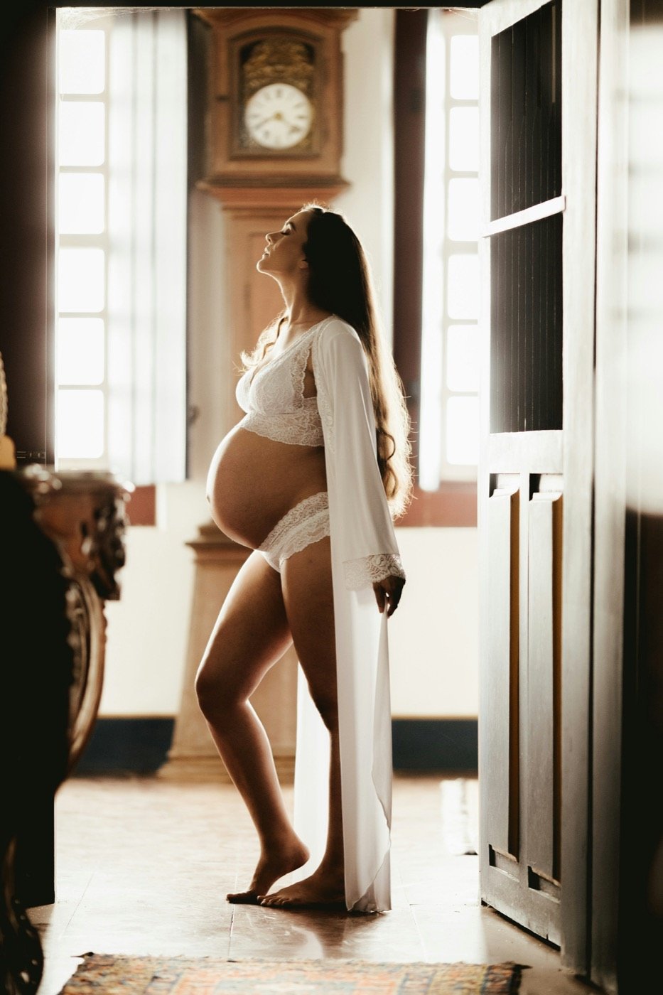 Expectant mother in white standing in warm window light