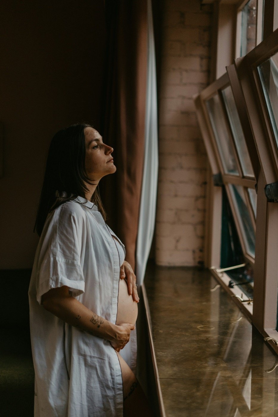 Expectant mother standing thoughtfully beside a window