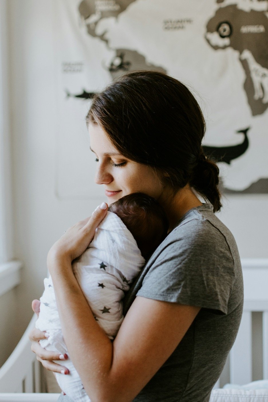 Mother holding her wrapped newborn close beside a window