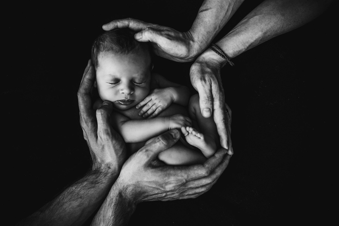 Newborn held safely within the hands of family members