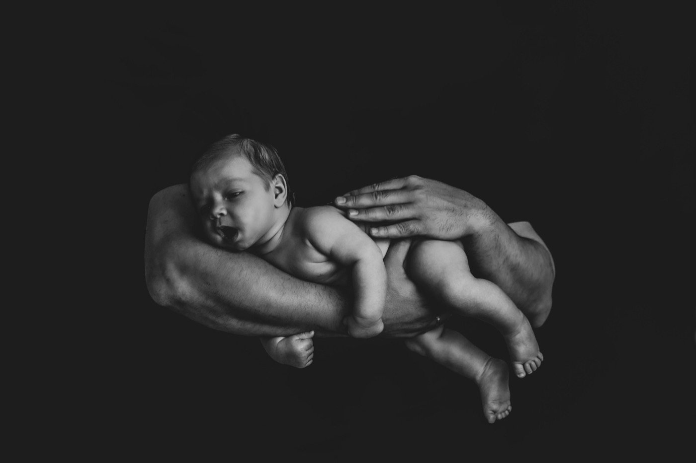 Black-and-white portrait of a newborn resting across a parent's arms